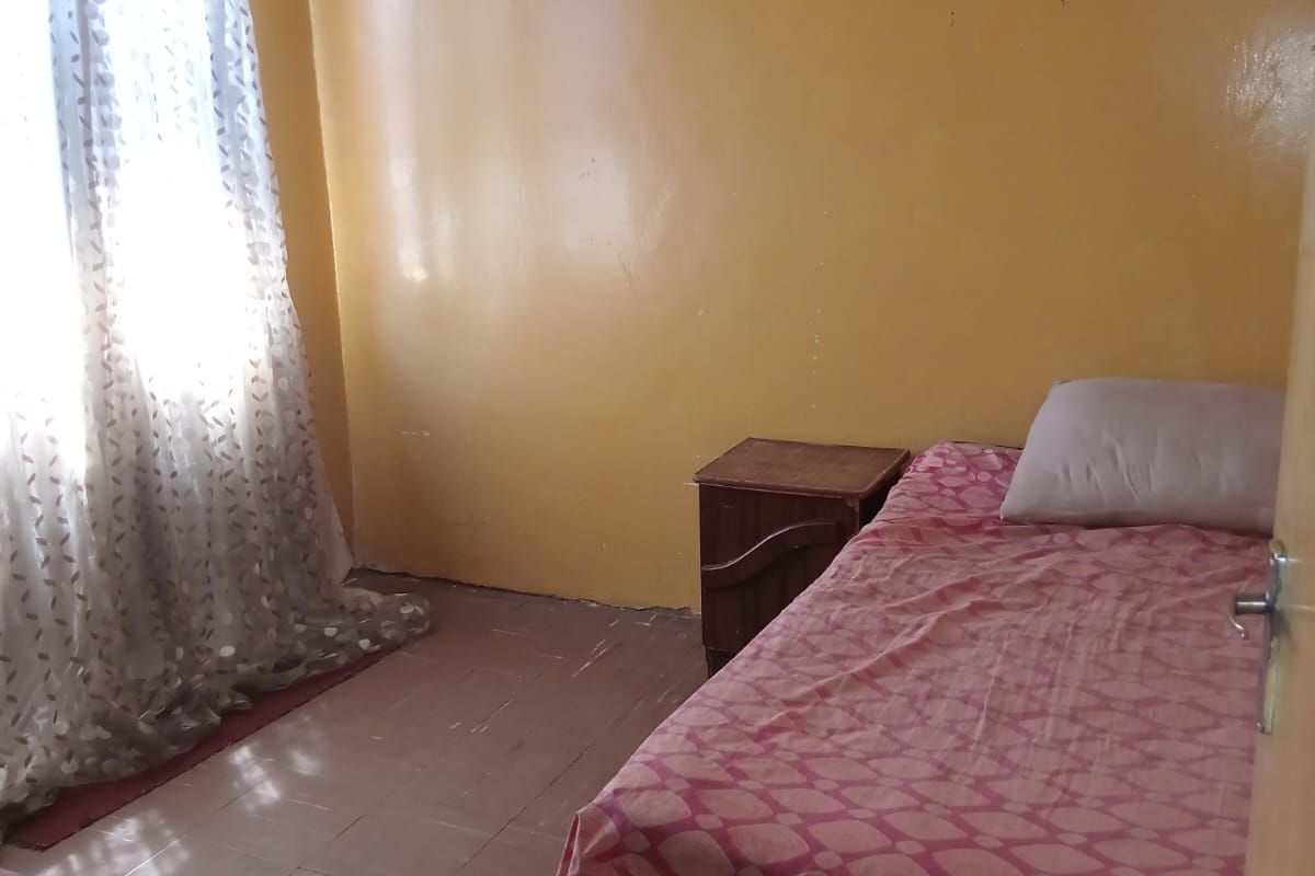 A simple bedroom featuring tiled flooring and yellow painted walls, offering a functional space ready for cosmetic updates.