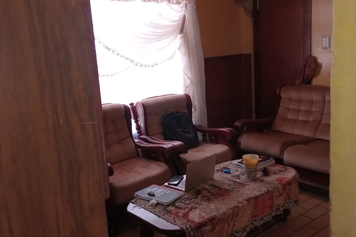 A living room featuring tiled flooring, a ceiling fan, and dated wall finishes, offering potential for modernization and aesthetic improvement.