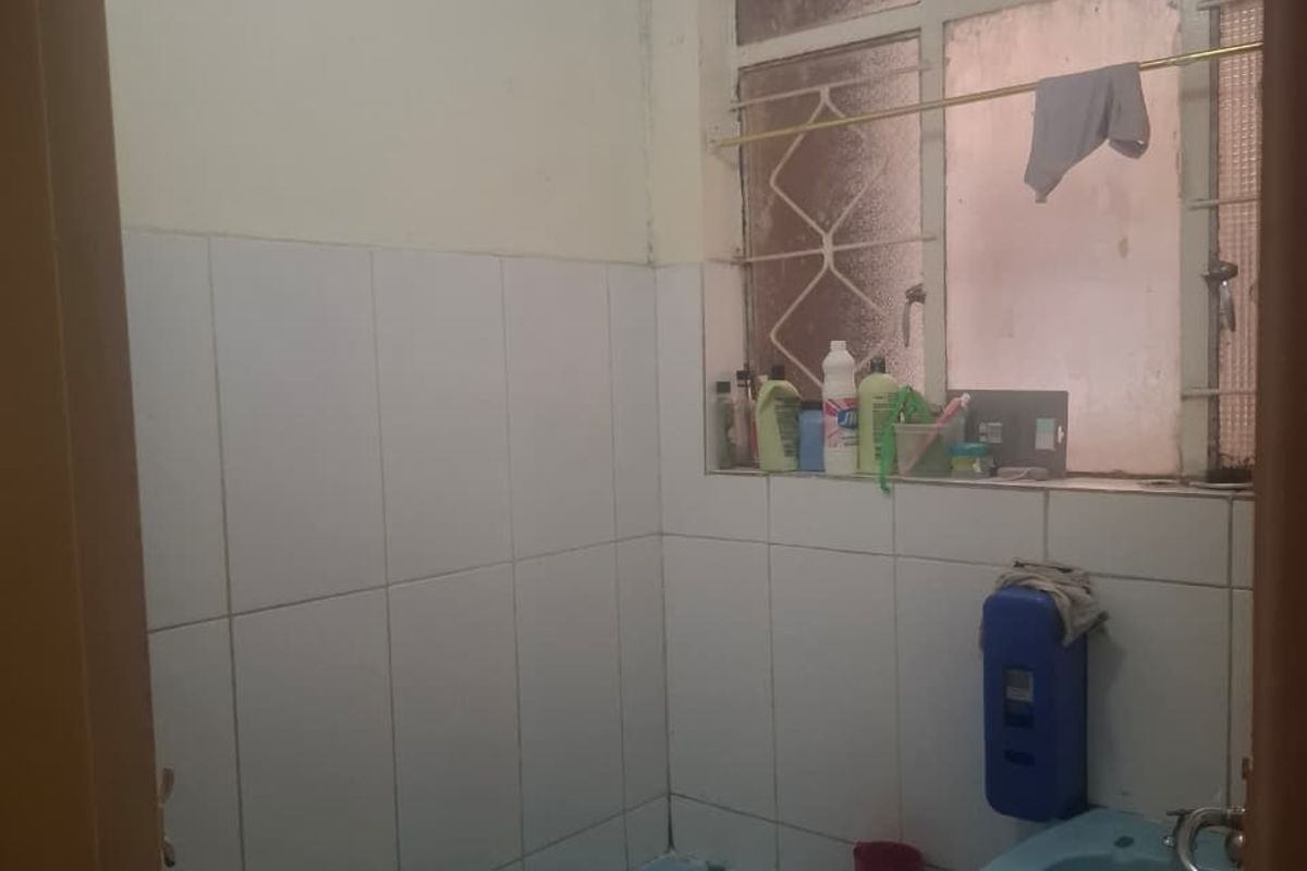 A dated bathroom featuring blue sanitaryware, tiled walls, and a window with security bars, requiring modernization to improve its aesthetic and functionality.