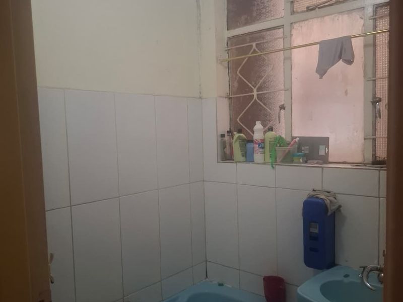 A dated bathroom featuring blue sanitaryware, tiled walls, and a window with security bars, requiring modernization to improve its aesthetic and functionality.