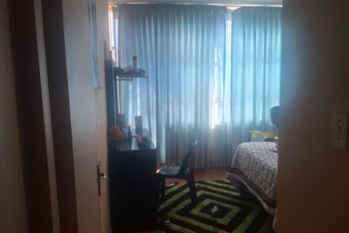 A bedroom featuring tiled flooring and large windows covered by curtains, viewed from the doorway.