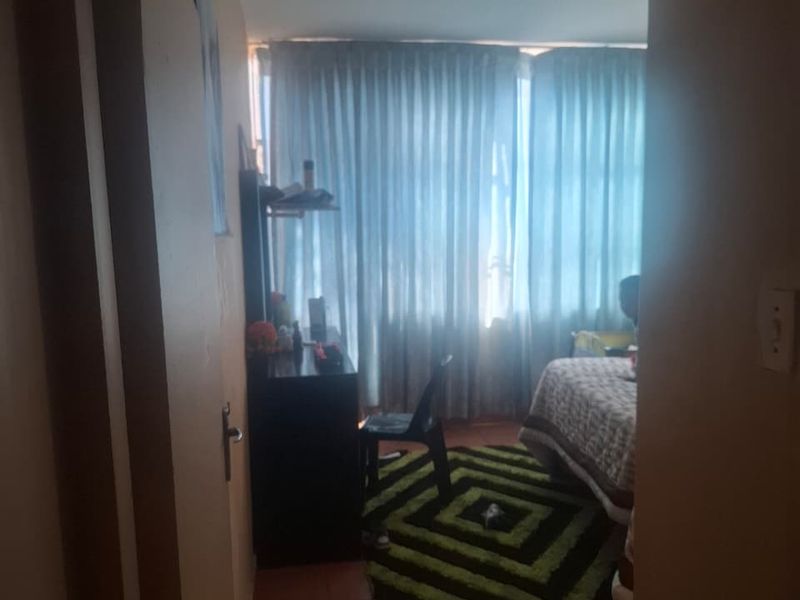 A bedroom featuring tiled flooring and large windows covered by curtains, viewed from the doorway.