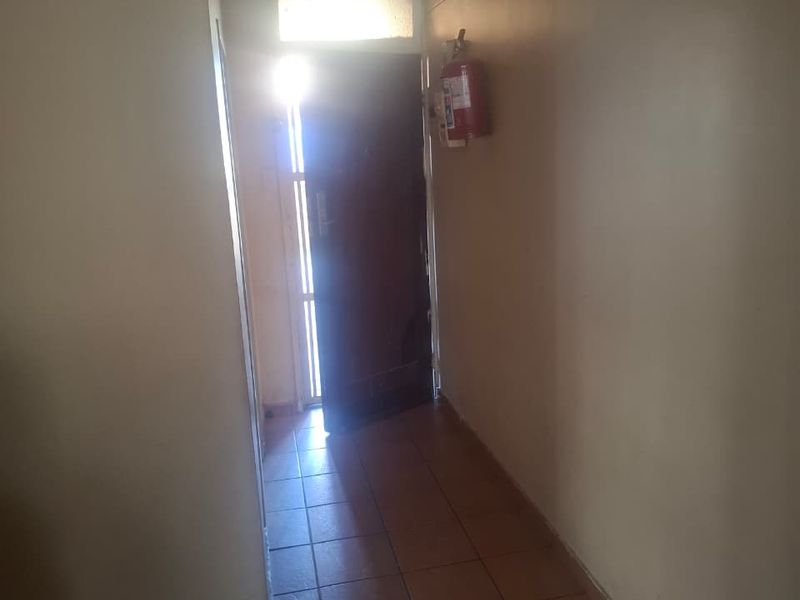 A functional apartment hallway featuring tiled flooring and a wall-mounted fire extinguisher, leading to the main entrance.