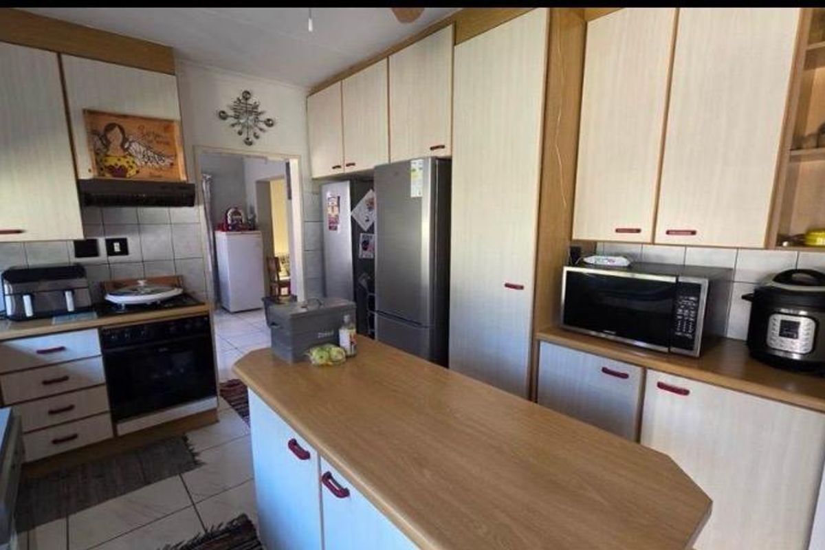 A functional kitchen featuring light-toned cabinetry, laminate countertops, a central island, and tiled flooring, offering a practical layout for daily meal preparation.