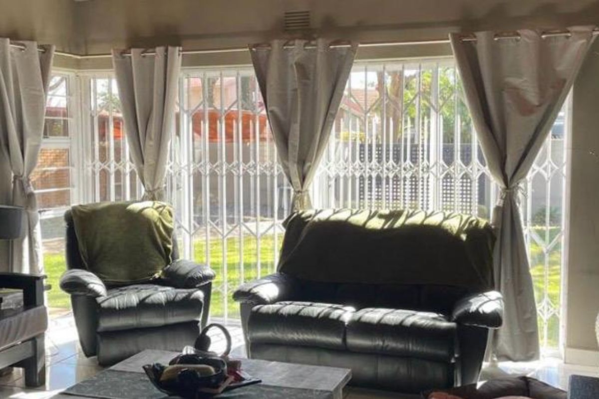 A living room featuring tiled flooring and a large sliding door secured with a white metal security gate, allowing natural light into the space.