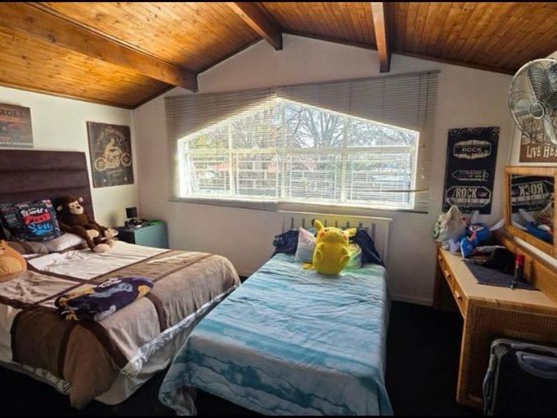 A bedroom featuring a vaulted timber ceiling with exposed beams, a large window providing natural light, and a wall-mounted fan.
