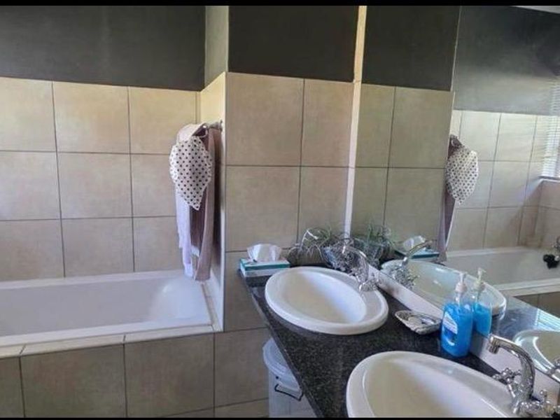 A functional bathroom featuring a double vanity with granite countertops, tiled walls, and a built-in bathtub.