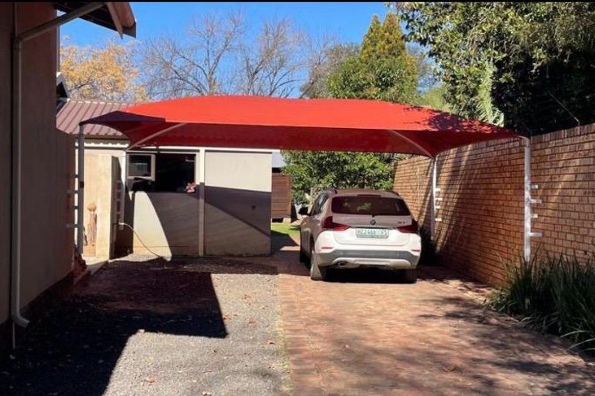 Rear exterior area featuring a paved driveway, a red shade sail carport, and a brick boundary wall.