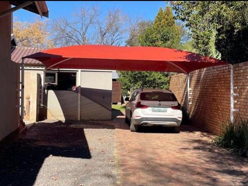 Rear exterior area featuring a paved driveway, a red shade sail carport, and a brick boundary wall.
