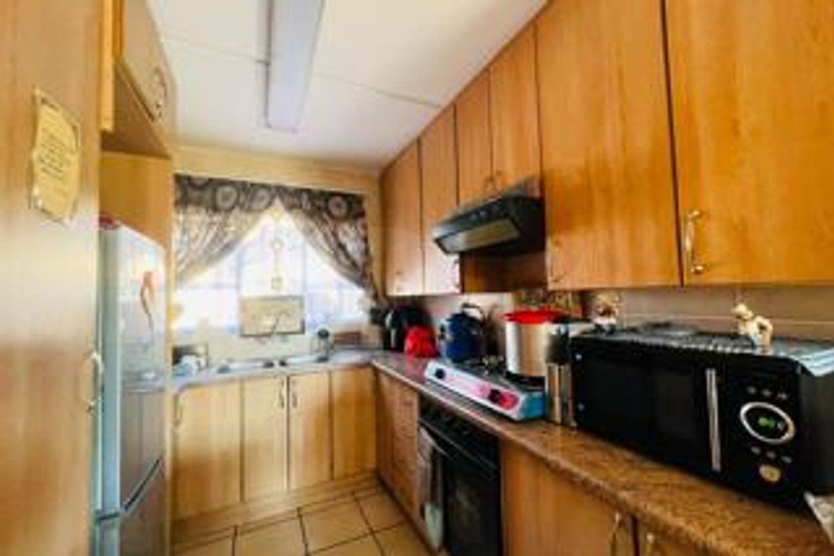 A functional kitchen featuring wood-tone cabinetry, laminate countertops, a double basin sink, and tiled flooring, offering a practical layout for daily meal preparation.