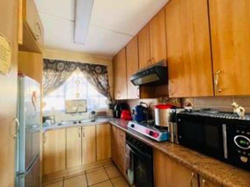 A functional kitchen featuring wood-tone cabinetry, laminate countertops, a double basin sink, and tiled flooring, offering a practical layout for daily meal preparation.