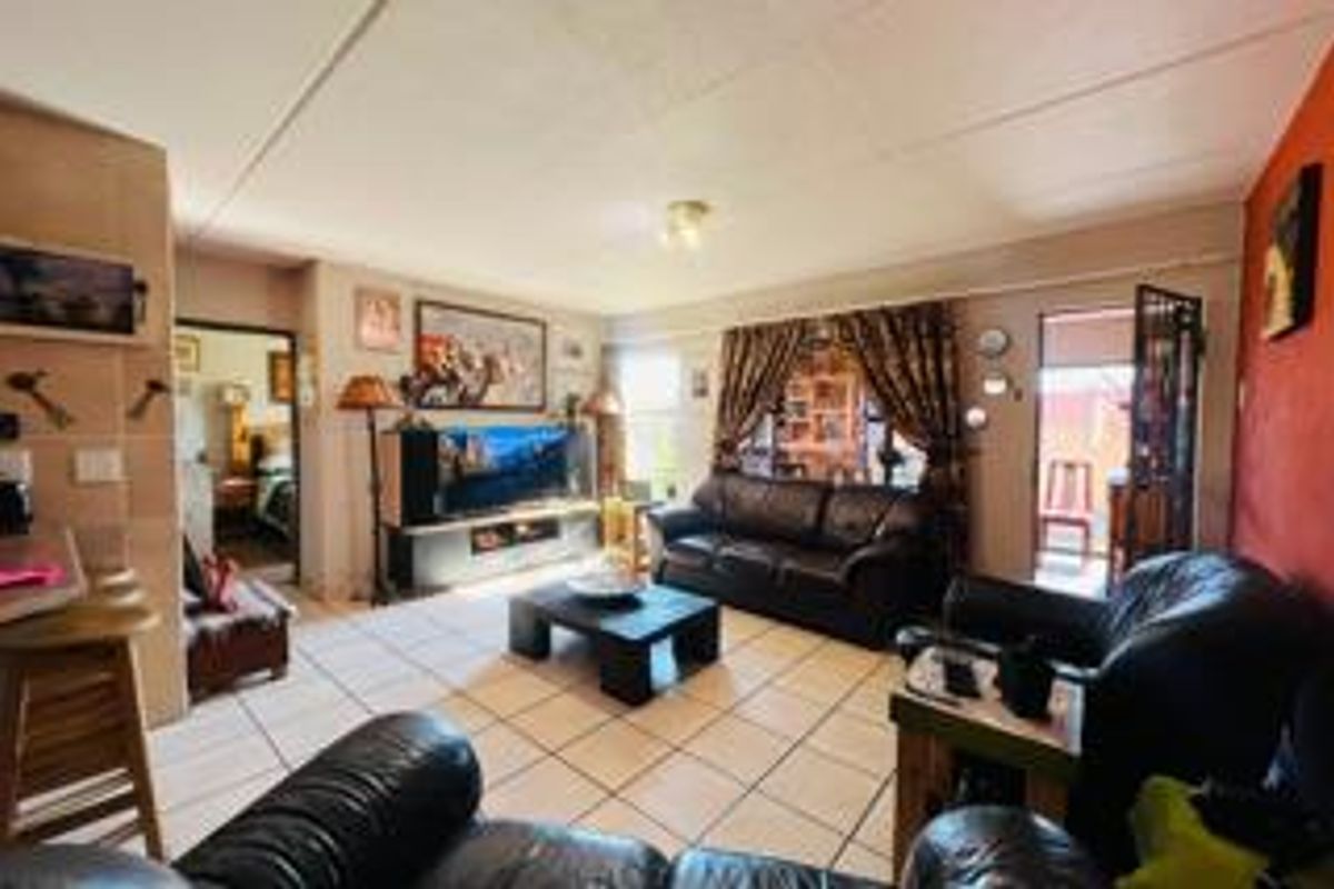 A spacious living room featuring tiled flooring and direct access to an outdoor area through a security gate and sliding door.