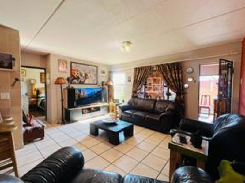 A spacious living room featuring tiled flooring and direct access to an outdoor area through a security gate and sliding door.