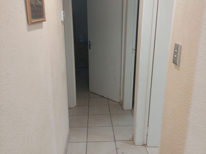A functional residential hallway featuring neutral tiled flooring and multiple internal doorways providing access to adjacent rooms.