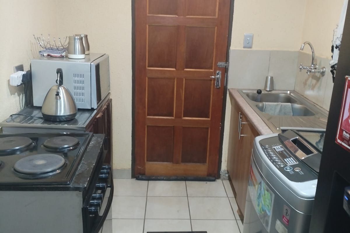 A compact kitchen area featuring tiled flooring, built-in cabinetry, a sink, and a wooden door leading to the exterior.