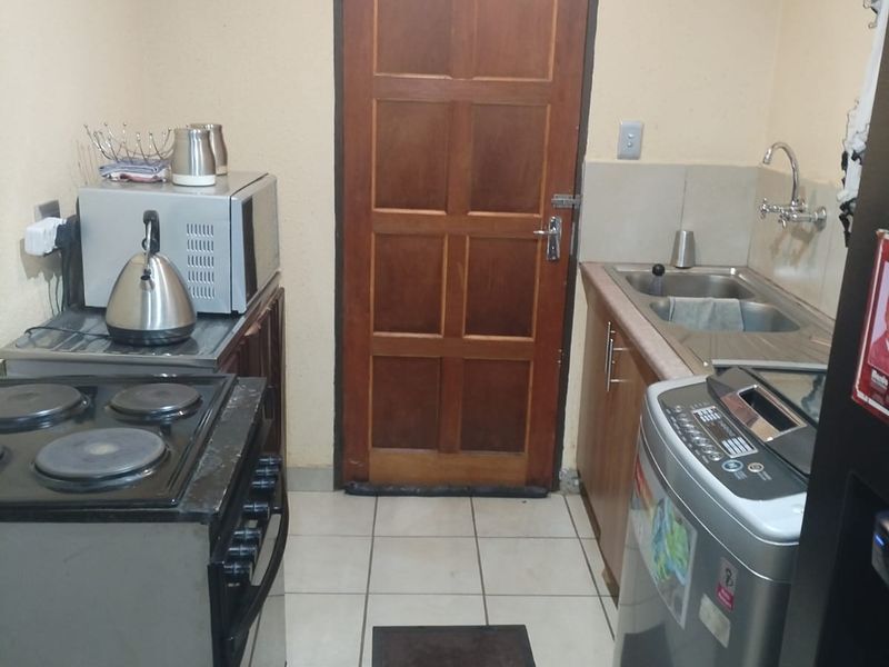 A compact kitchen area featuring tiled flooring, built-in cabinetry, a sink, and a wooden door leading to the exterior.