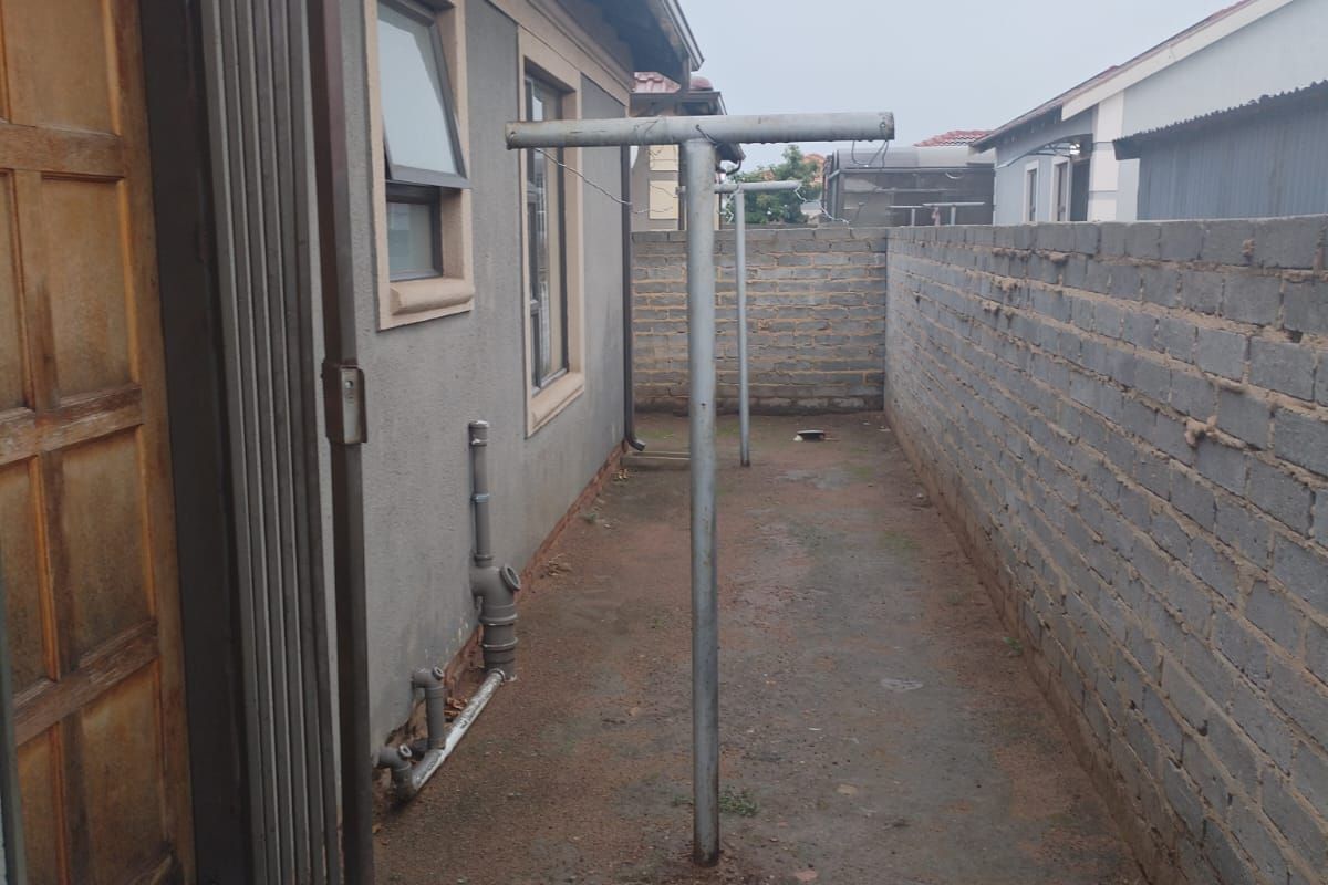 A narrow rear exterior side passage featuring a metal washing line, exposed brick boundary wall, and direct access to the home via a timber door.