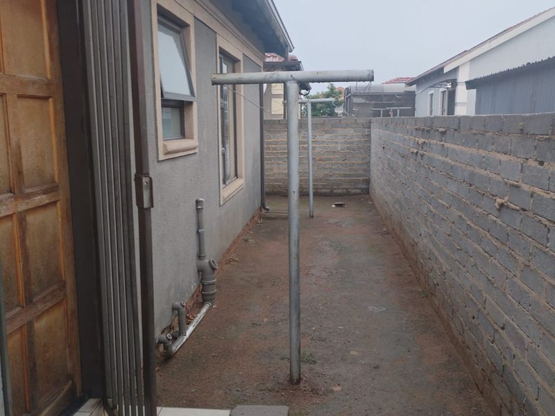 A narrow rear exterior side passage featuring a metal washing line, exposed brick boundary wall, and direct access to the home via a timber door.