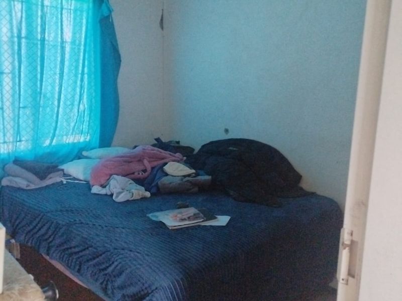 A bedroom featuring tiled flooring and a window with security bars, showing signs of wall plaster damage near the ceiling corner.