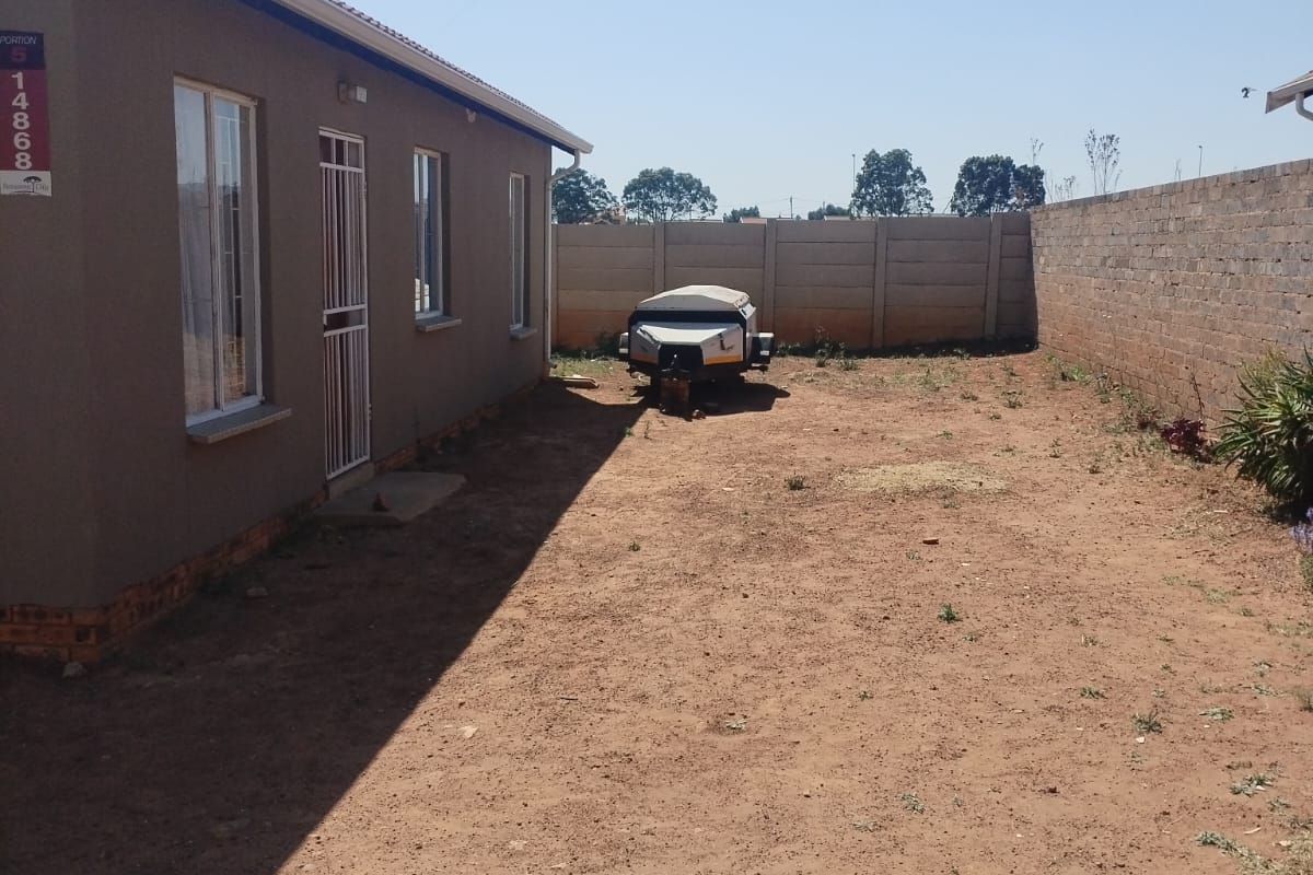 Rear exterior view of the property featuring a large, unlandscaped yard enclosed by a precast concrete boundary wall.