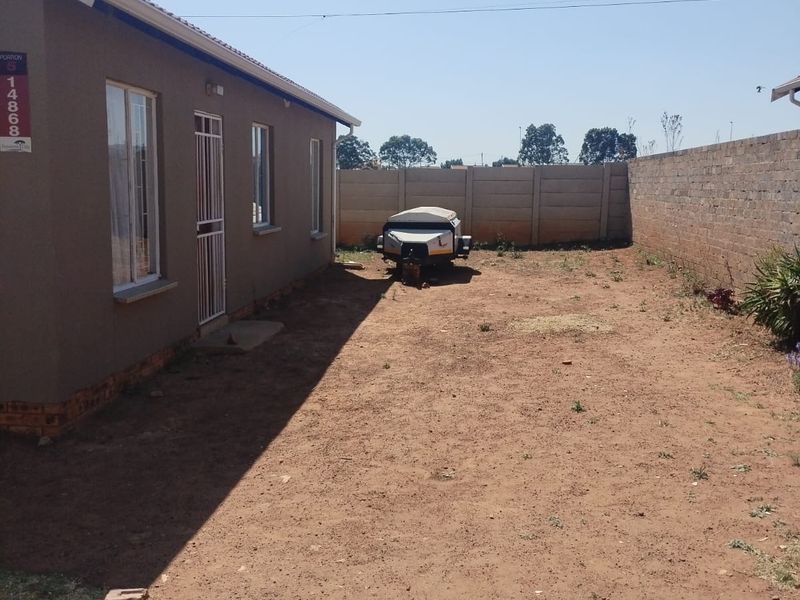 Rear exterior view of the property featuring a large, unlandscaped yard enclosed by a precast concrete boundary wall.