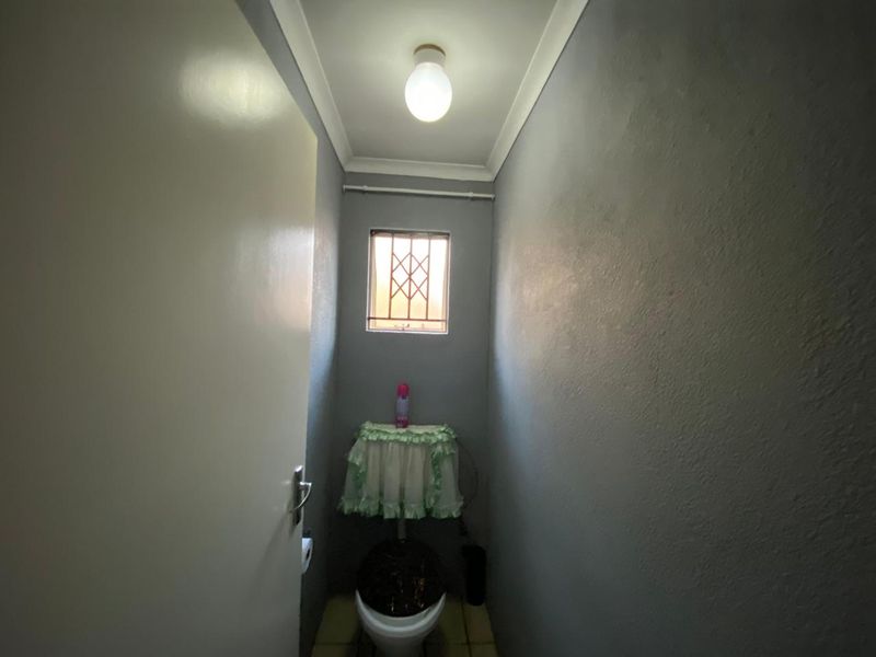 A compact guest toilet featuring grey painted walls, a small window with a security gate, and standard sanitary fixtures.