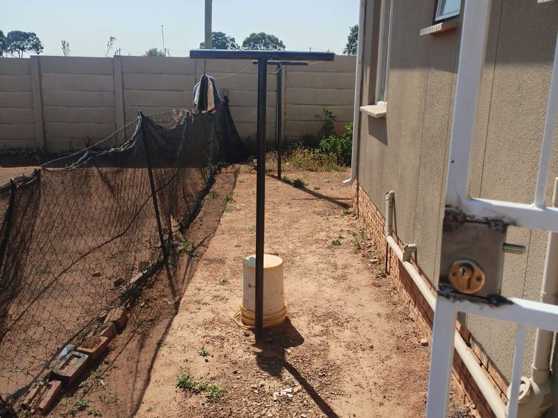 Rear exterior area featuring a precast concrete boundary wall, metal washing line, and unpaved ground, offering potential for landscaping or patio development.