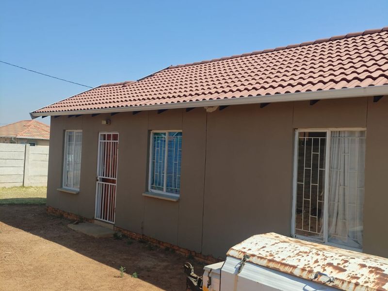 Rear view of a single-story house featuring a tiled roof, security bars on windows, and a security gate entrance.