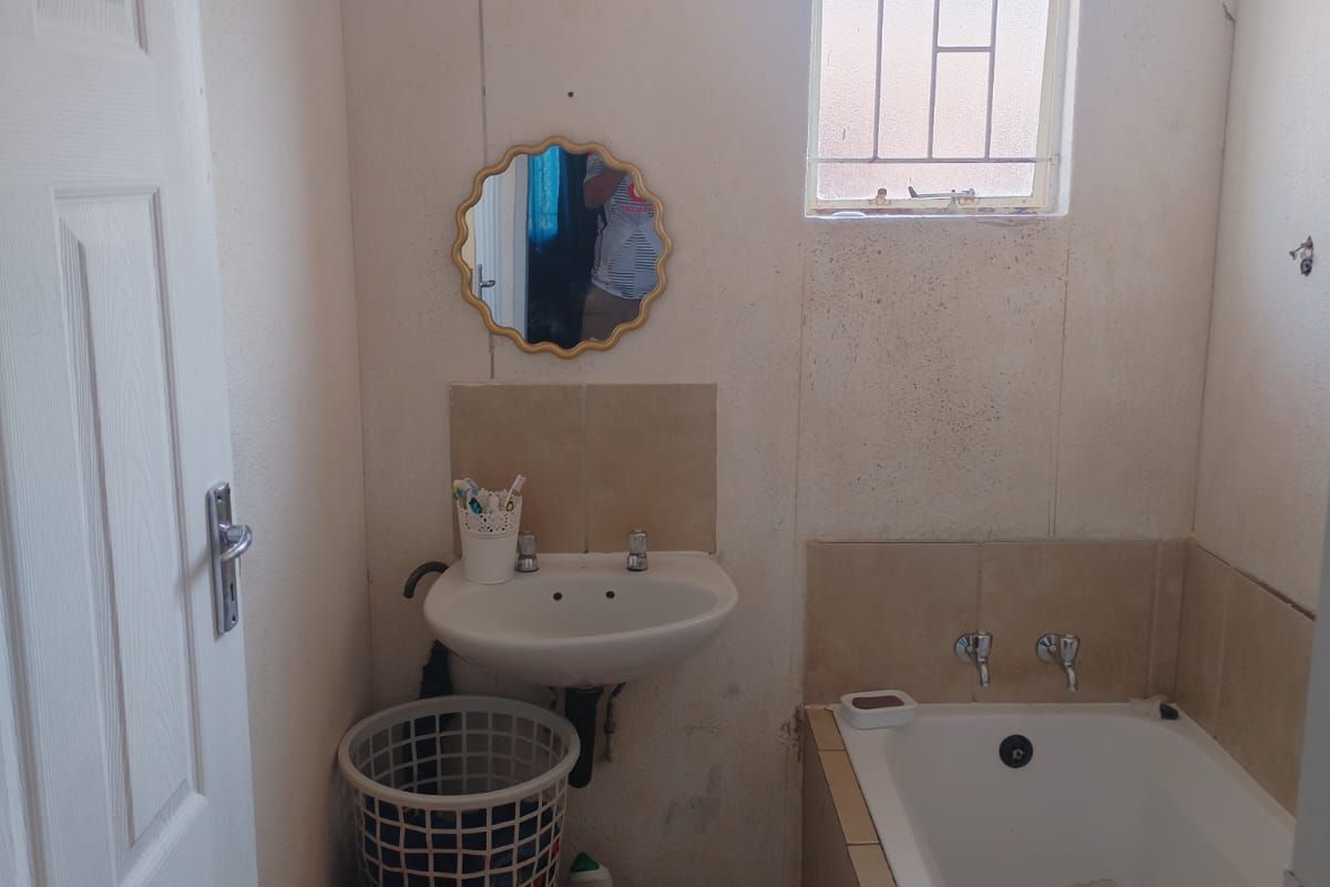 A compact bathroom featuring a wall-mounted basin, built-in bathtub, and tiled flooring. The space requires cosmetic updates to improve its overall condition.
