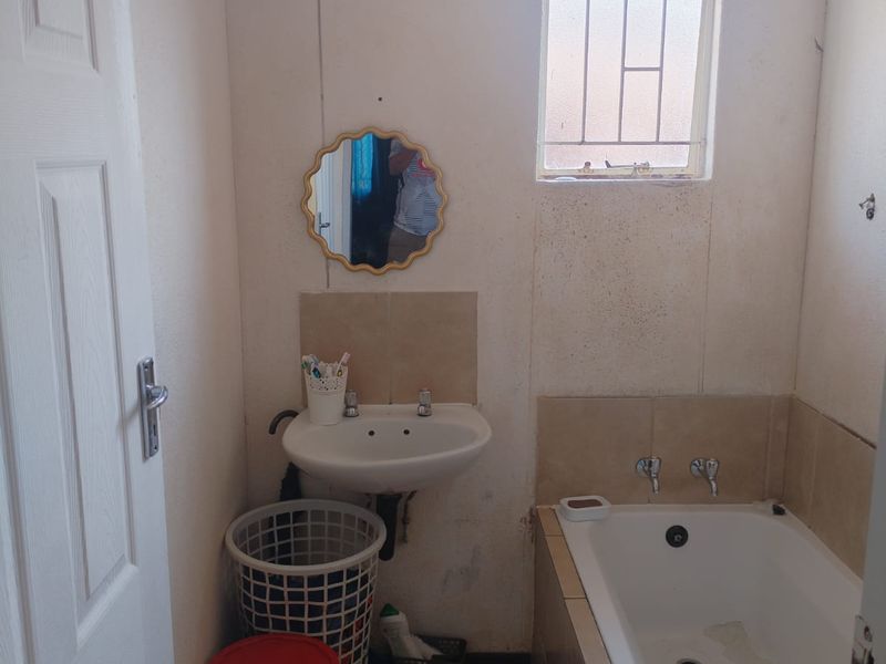 A compact bathroom featuring a wall-mounted basin, built-in bathtub, and tiled flooring. The space requires cosmetic updates to improve its overall condition.
