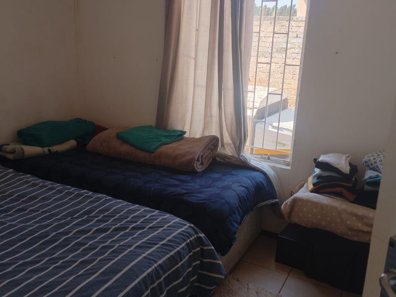 A compact bedroom featuring tiled flooring and a window fitted with security bars, offering natural light.