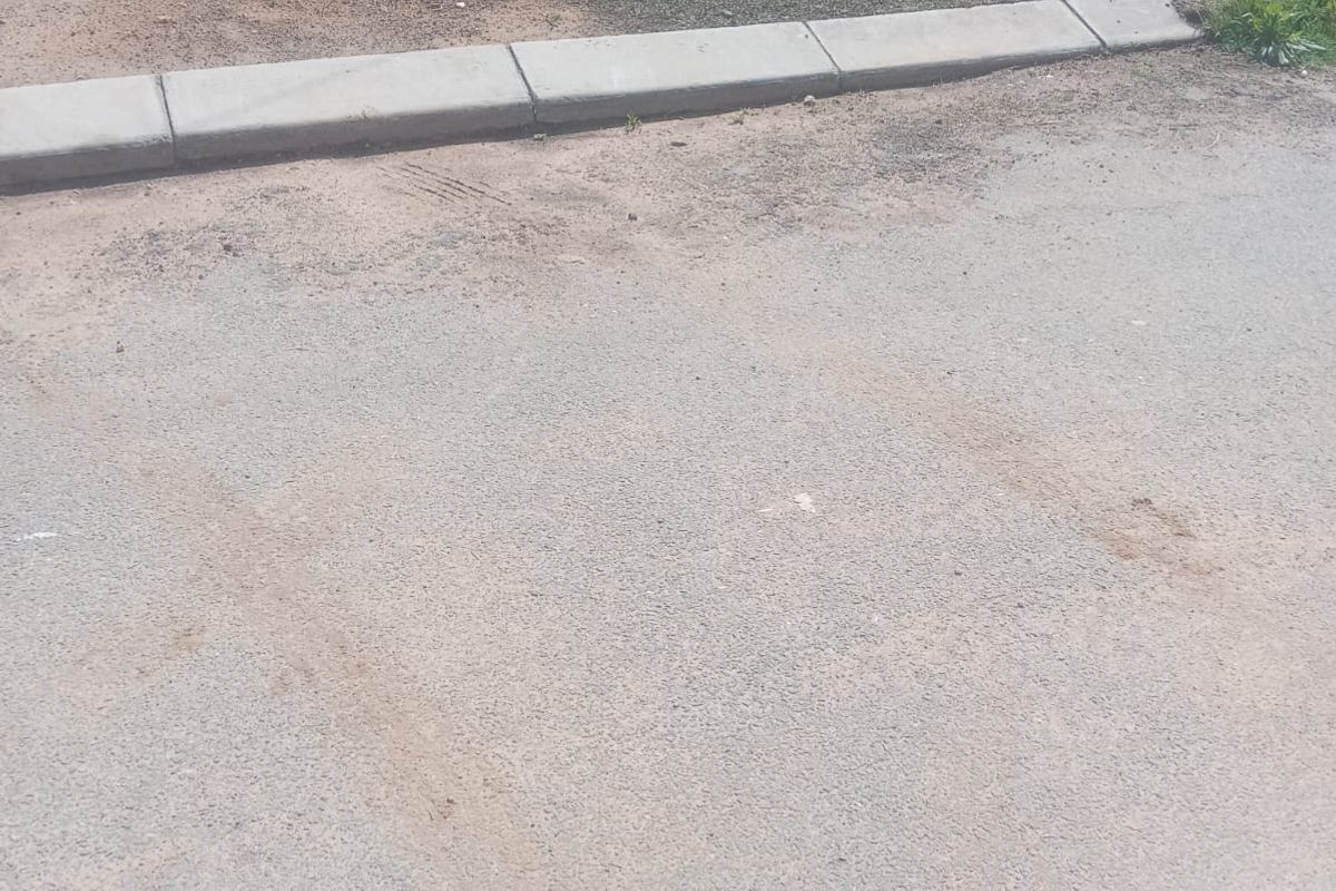 A view of the street frontage showing the asphalt road surface and concrete kerbing bordering the vacant residential land.