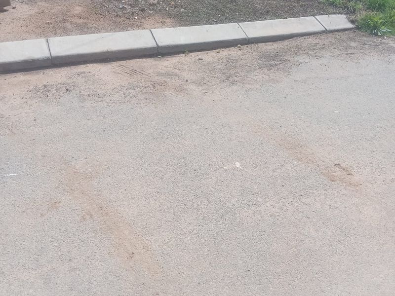 A view of the street frontage showing the asphalt road surface and concrete kerbing bordering the vacant residential land.