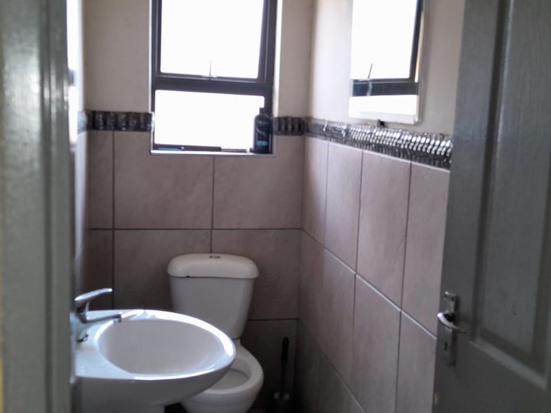 A compact bathroom featuring a pedestal basin, toilet, and tiled walls with a decorative border.
