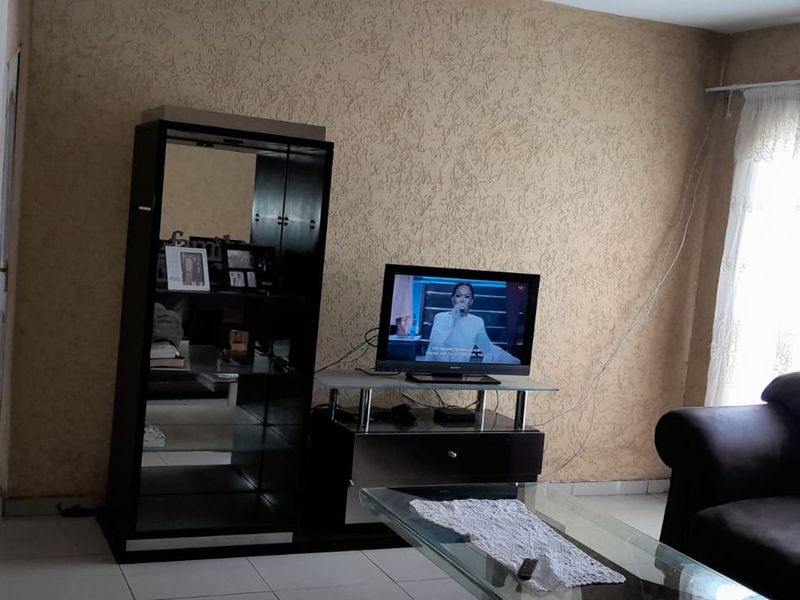 A living room area featuring tiled flooring and textured wall finishes, providing a functional space with access to an adjacent hallway.