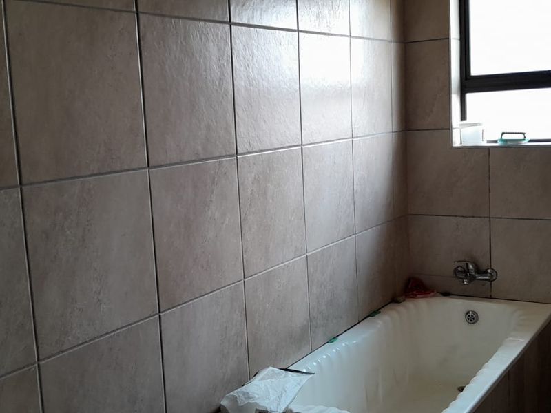 A functional bathroom featuring full-height wall tiling, a built-in bathtub, and a window for natural light.