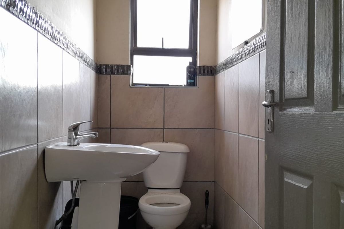 A compact bathroom featuring a pedestal washbasin, toilet, and neutral wall tiling with a decorative border.
