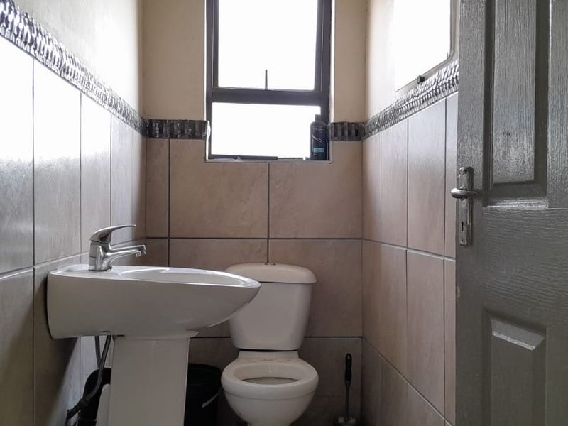 A compact bathroom featuring a pedestal washbasin, toilet, and neutral wall tiling with a decorative border.