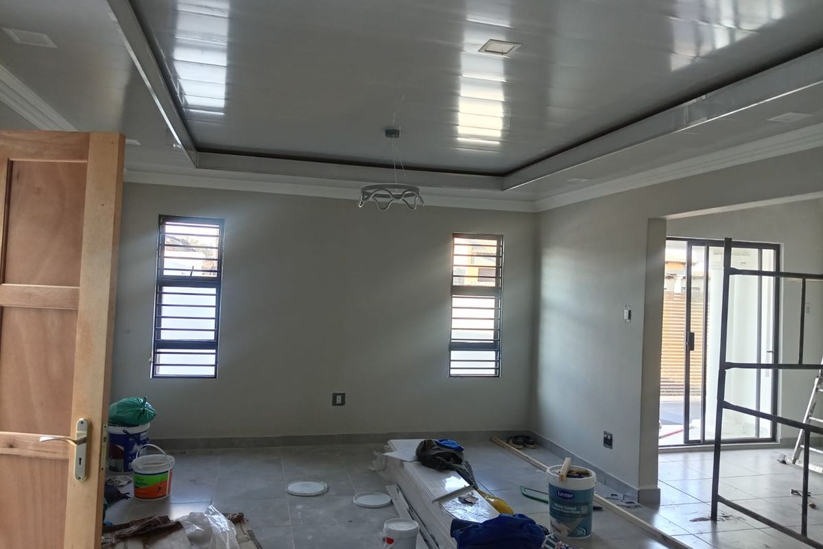 Spacious living area currently under final construction, featuring tiled floors, recessed ceiling details, and large windows providing natural light.