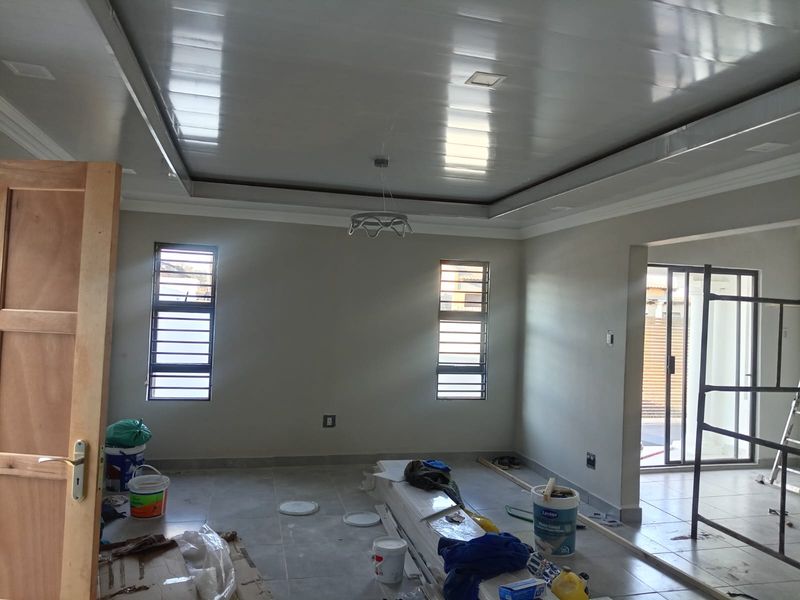 Spacious living area currently under final construction, featuring tiled floors, recessed ceiling details, and large windows providing natural light.