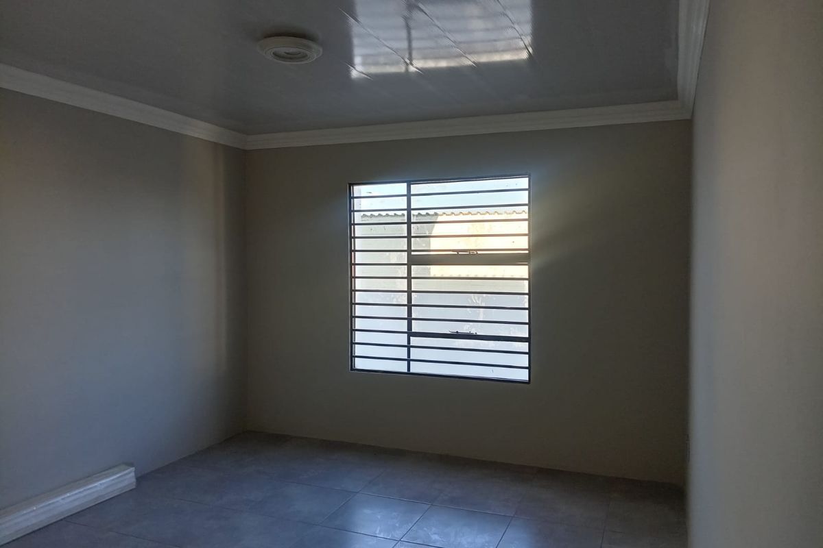A clean, empty bedroom featuring neutral tiled flooring, a glossy ceiling finish, and a window fitted with security bars.