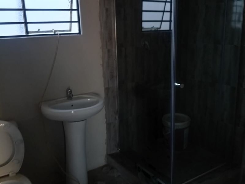 A bathroom in the process of renovation featuring a pedestal basin, toilet, and a glass shower enclosure with unfinished wall tiling.