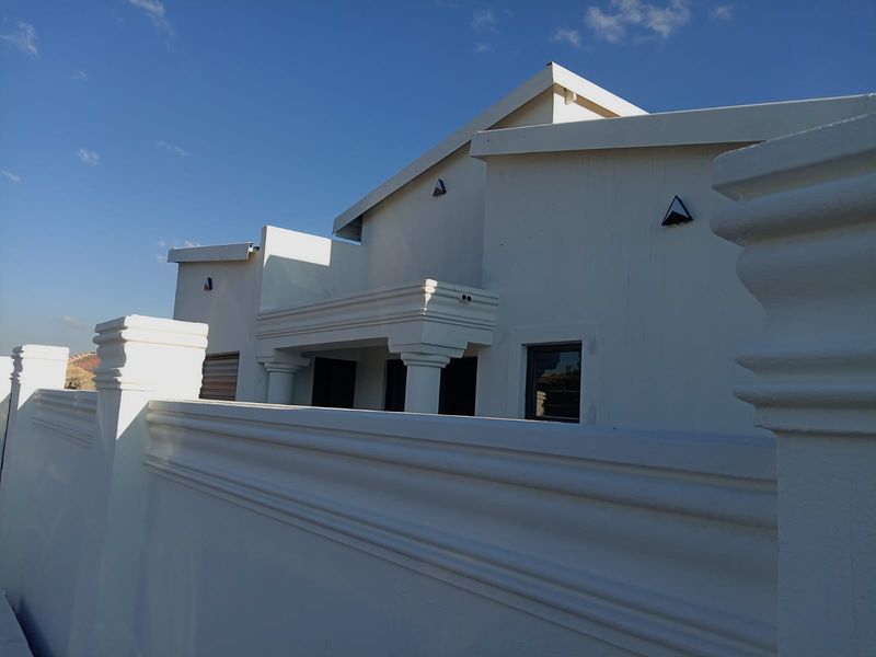 A modern residential exterior featuring a clean white facade, decorative perimeter wall, and gabled roof architecture under a clear blue sky.