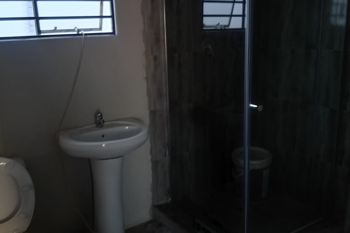 A bathroom in the process of renovation featuring a pedestal basin, toilet, and a glass shower enclosure with unfinished wall tiling.