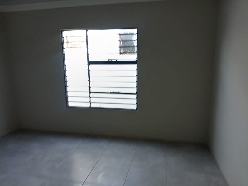 An empty bedroom featuring tiled flooring and a louvered window, providing a blank canvas for interior design.