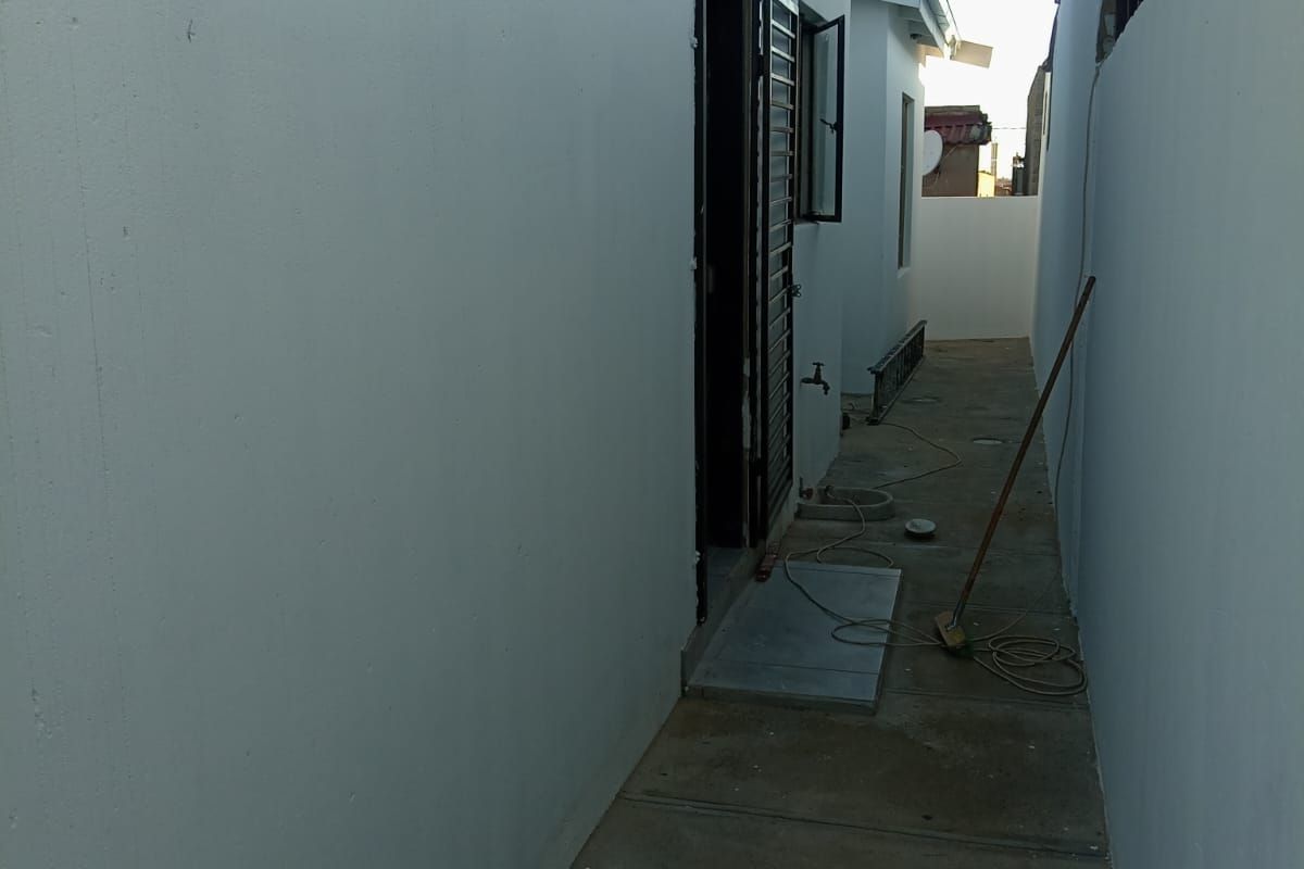 A narrow side passage or rear exterior walkway featuring a concrete path, external water tap, and access to the building via a security gate.