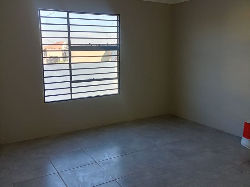 A clean, empty bedroom featuring neutral wall paint, tiled flooring, and a window fitted with security bars.