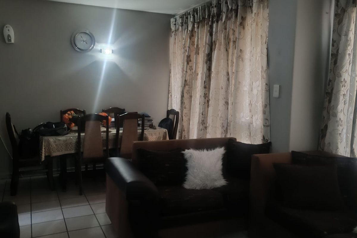 A living and dining area featuring tiled flooring and large windows with curtain tracks, providing a functional space for relaxation and meals.
