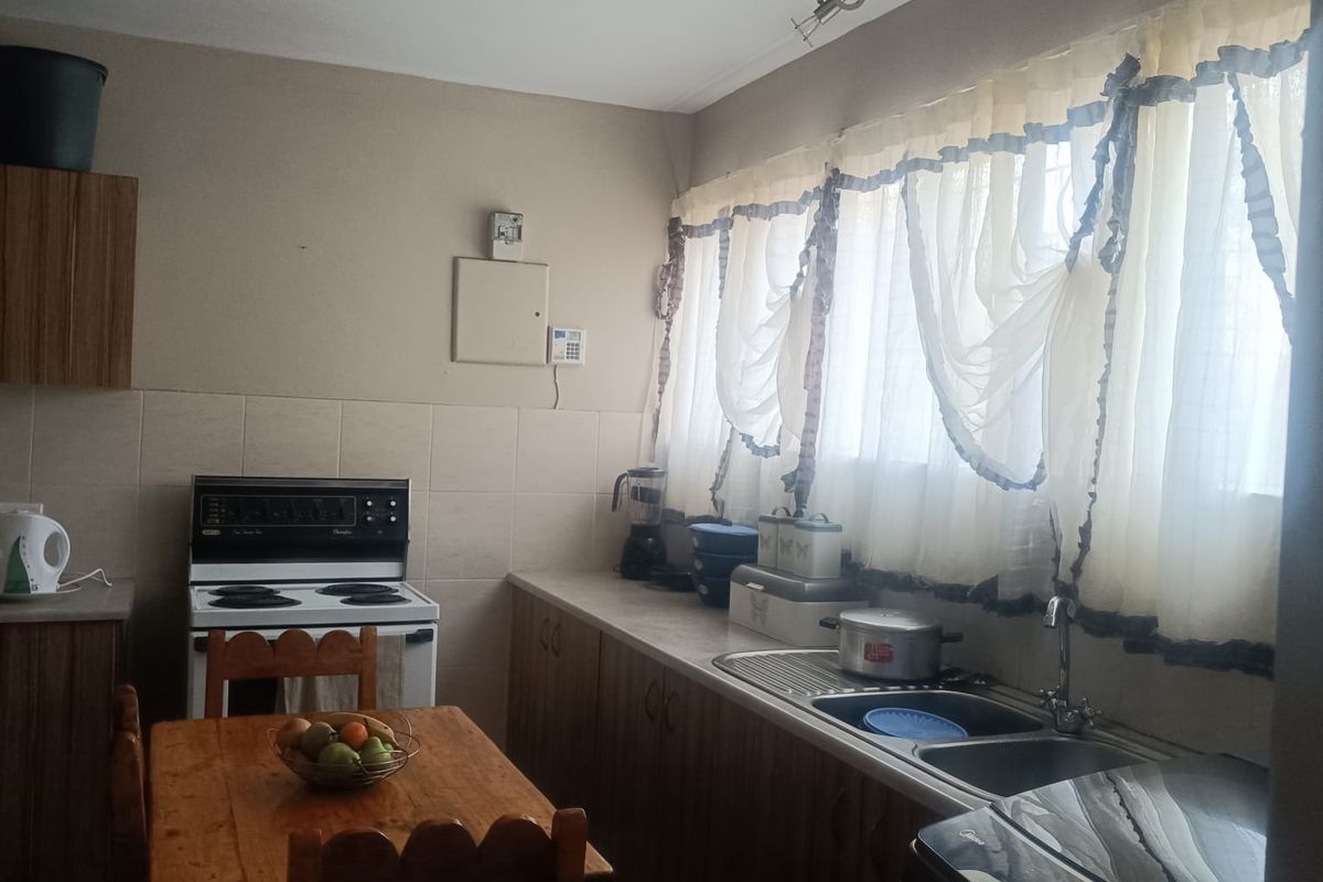 A functional kitchen featuring built-in wooden cabinetry, a stainless steel sink, tiled backsplash, and a freestanding stove with tiled flooring.