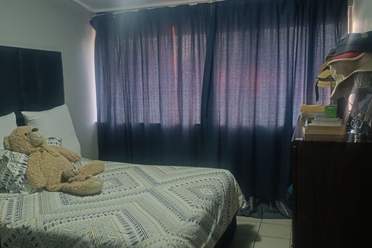 A functional bedroom featuring tiled flooring and a large window with dark curtains, providing a simple and practical living space.
